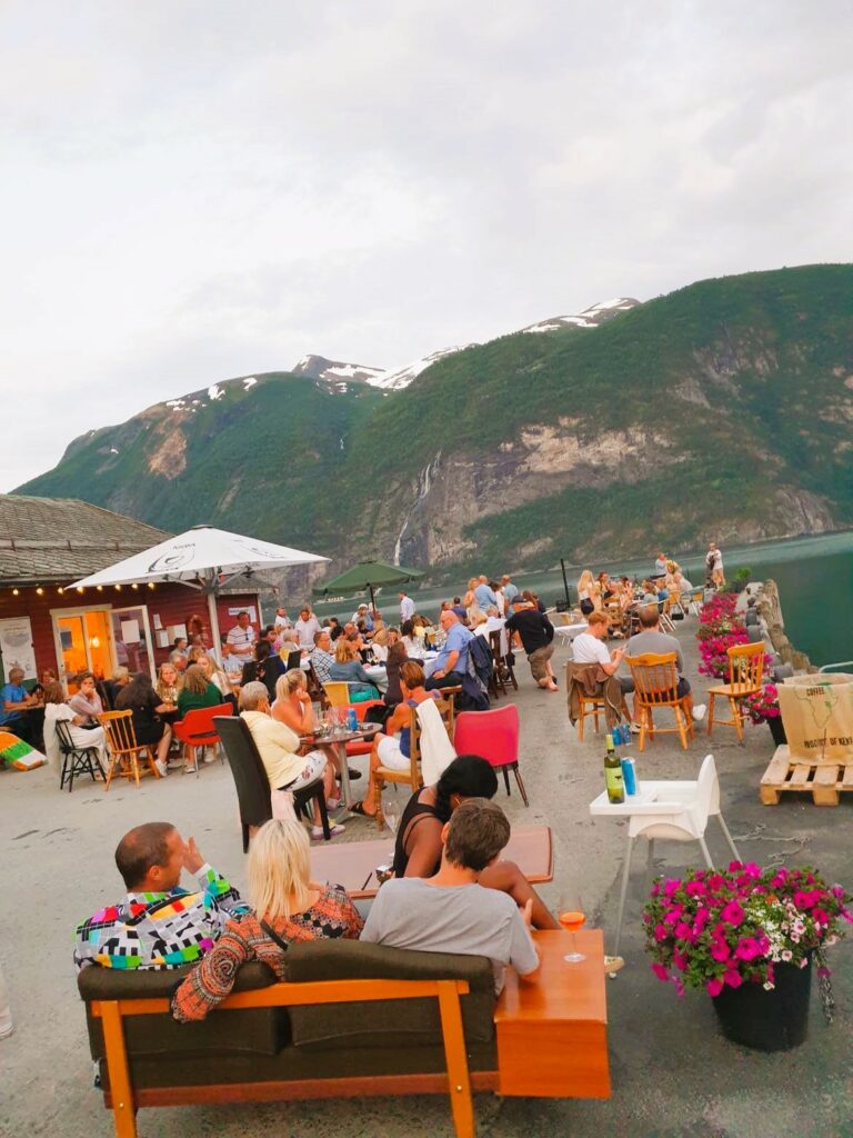 Mennesker koser seg utenfor Khaya Barista bar i Valldal med fjord og fjell i bakgrunn